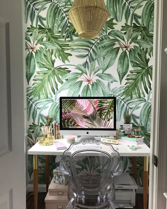 a small tropical home office with a tropical accent wall, a rattan lamp, a sheer chair, touches of gold here and there