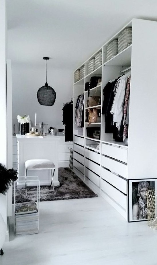 a small white closet with holders, shelves and lots of drawers, with a tiny table for makeup and a black pendant lamp