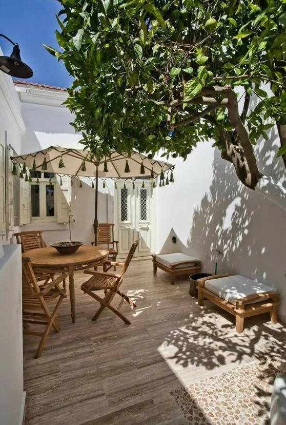 a small yet cool patio done Mediterranean style with a deck, a wooden dining set, a couple of seats and a living tree
