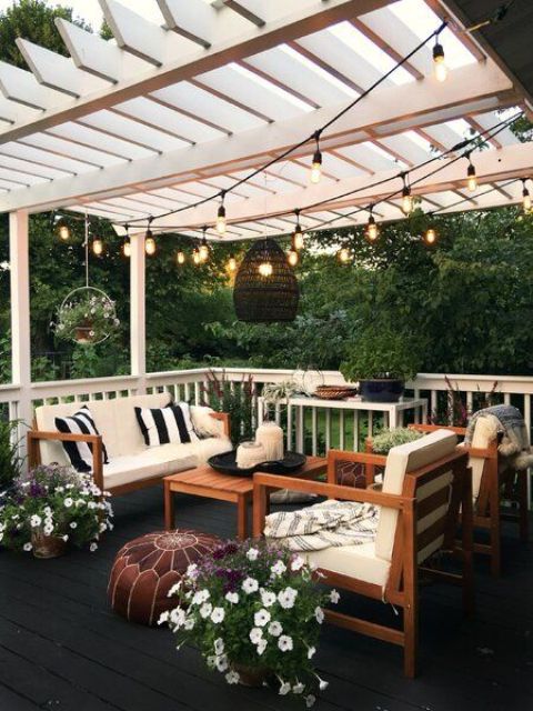 a small yet cozy patio with a sofa and chairs, a leather ottoman, potted blooms and greenery, lights and candle lanterns