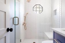 a small yet stylish bathroom with catchy long tiles in the shower and patterned ones ont he floor, with a bold blue vanity, brass touches and a geometric window