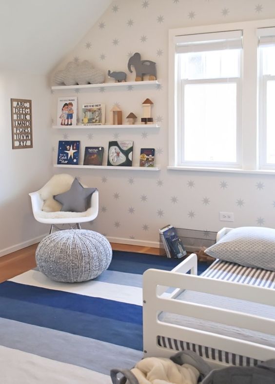 a starry nursery with a star printed wall, blue textiles, an open shelf and lots of toys and books