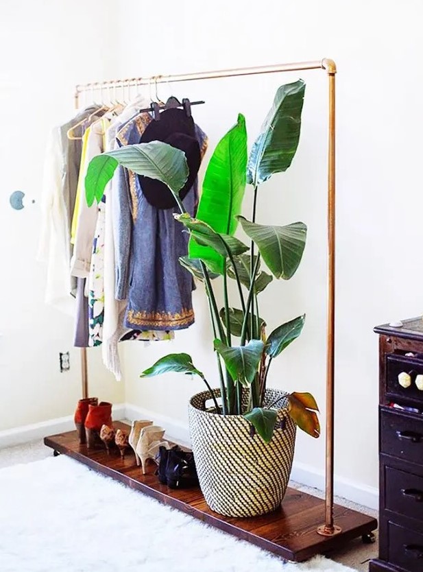 a stylish makeshift closet with a metal and stained wood rack for clothes and shoes and a dark-stained dresser plus a potted plant