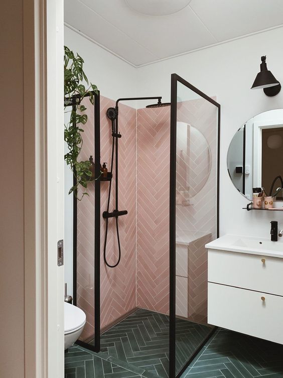 a stylish small bathroom with green herringbone tiles on the floor, pink ones in the shower, a floating vanity and black framing