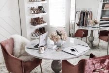 a super glam cloffice with an oversized mirror, a crystal chandelier, dusty pink velvet chairs, a vintage table and open shelves for shoes