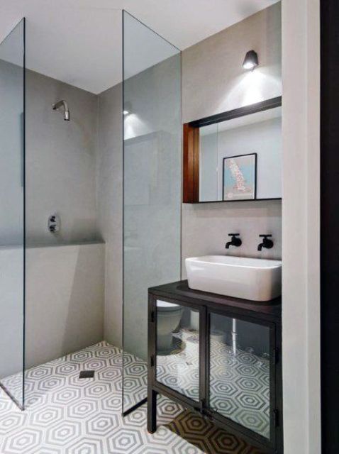 a tiny bathroom with concrete walls and printed tiles on the floor, a small shower space, a black vanity and a sink