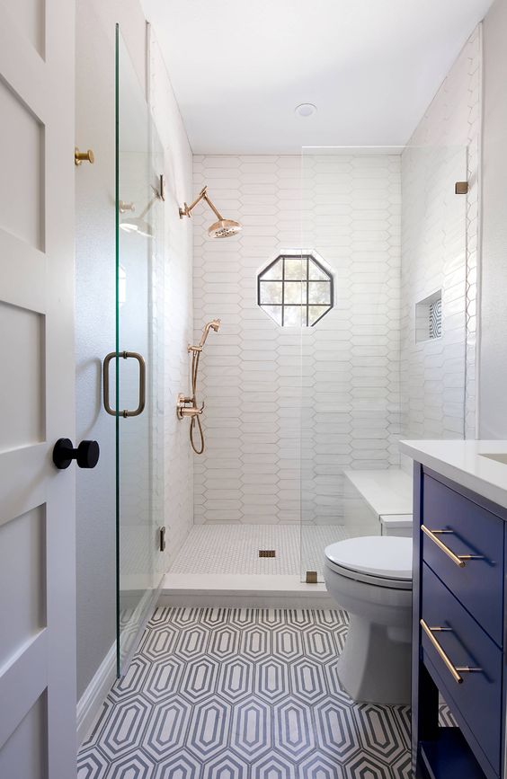 a tiny bathroom with white and printed tiles, a navy vanity, white appliances, brass fixtures and black touches