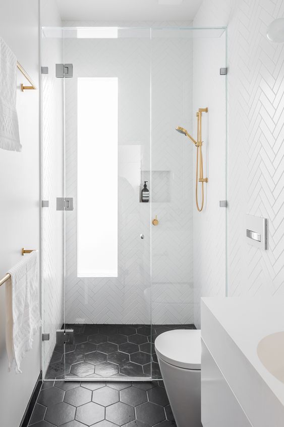 a tiny black and white bathroom with white herringbone tiles on the walls, black hexagon ones on the floor and gold fixtures