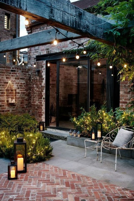 a tiny chic backyard clad with concrete and bricks, with greenery and lights and candle lanterns looks inviting