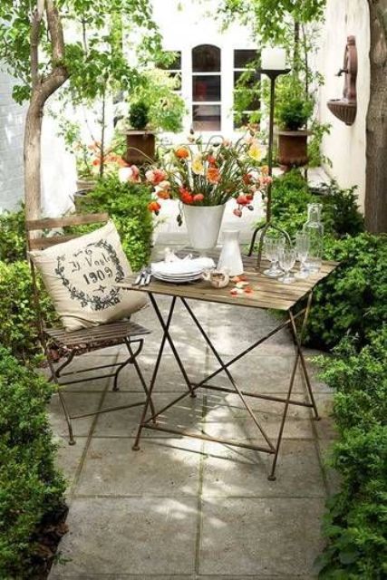 a tiny patio with a folding table and chair, lots of greenery lining up the patio and some trees