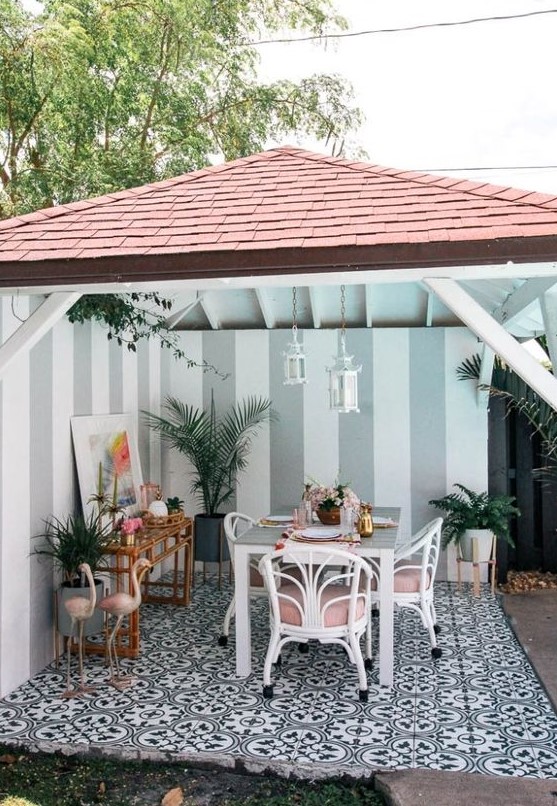 a tropical patio with a dining space done with white and pink rattan chairs, pink flamingos, a rattan bar table and potted plants