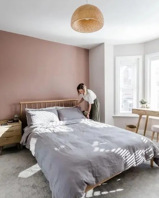 a welcoming and airy bedroom with a mauve accent wall, a wooden bed and wooden furniture, a rattan pendant lamp