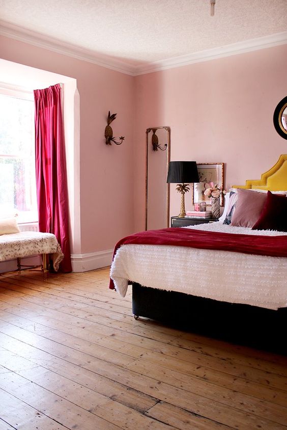 a whimsical bedroom with a bed with a yellow headboard and contrasting bedding, a mirror, black nightstands and lamps, a fuchsia curtain