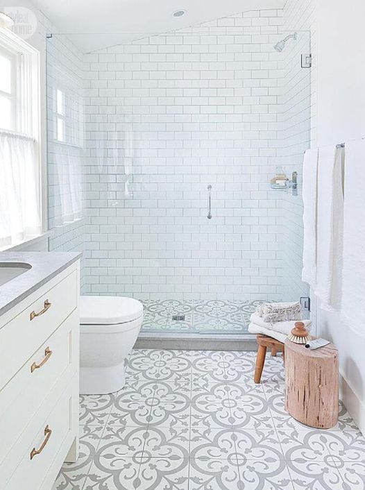 an airy neutral bathroom with white subway tiles and printed ones on the floor, a white vanity, a stool and a tree stump