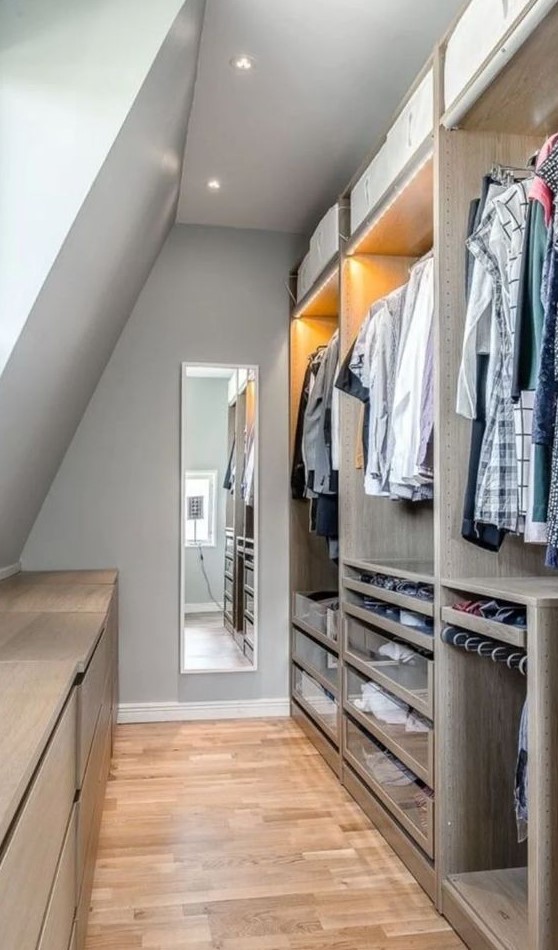 an attic closet with open storage compartments and lights, drawers and railing, several dressers and a long and tall mirror