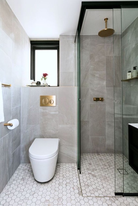 an elegant contemporary bathroom with stone and marble tiles, a window, a shower space and gilded touches