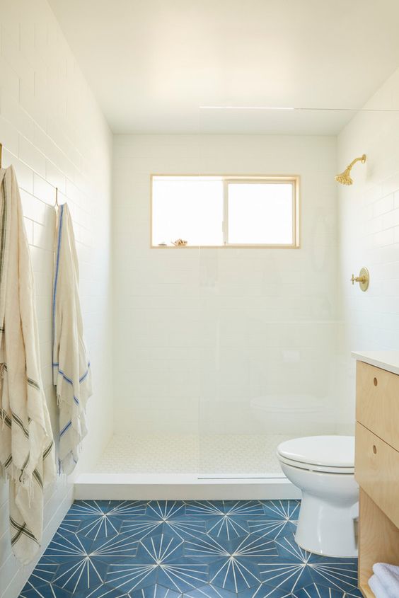 white tiles on the walls and ceilings, navy tiles on the floor, a light-colored wooden vanity and a small window is inviting