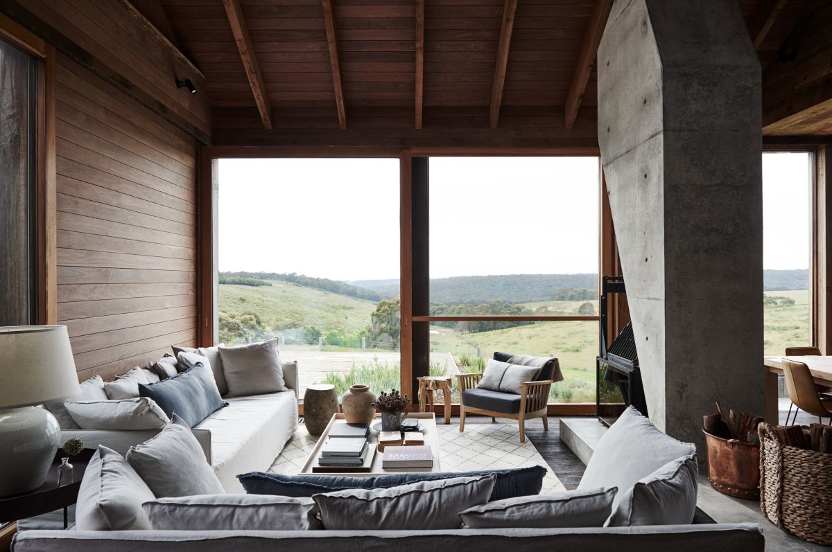 The living room features a glazed wall, wooden furniture and comfy sofas around a hearth cast in concrete