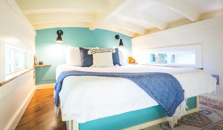 Upstairs there's a bedroom with small windows, an accent turquoise wall and a large comfy bed
