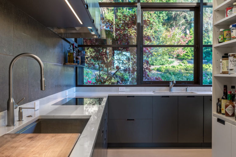 The kitchen is done with sleek graphite grey cabinets, white stone countertops and a glazed wall instead of a backsplash