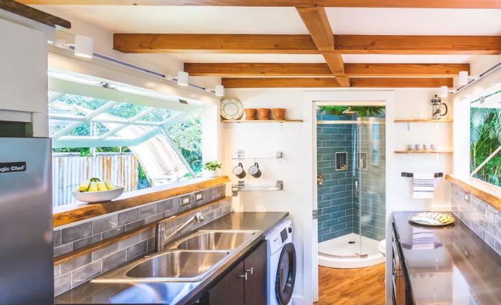 The kitchen features some windows, black cabinets and wooden beams on the ceiling