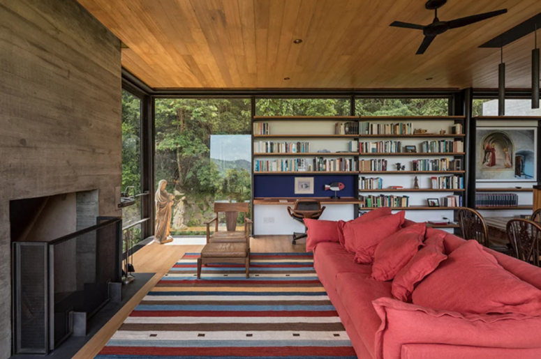The living room is done with a red sofa, a fireplace, a shelving unit, a desk and a striped rug