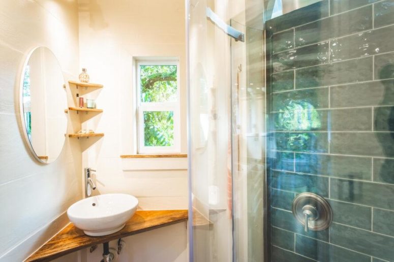 A tiny bathroom features a small sink in the corner, a small shower with tiles