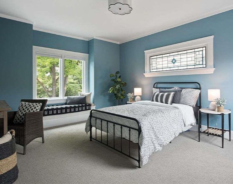 A guest bedroom is done in blue, with several windows, comfy metal and wicker furniture and monochromatic textiles