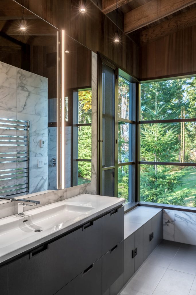 The bathroom is done with white marble tiles and sleek dark cabinets and a vanity, there are glazed walls here, too