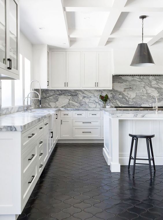 a neutral farmhouse kitchen with a white marble backsplash and countertops and black touches and a black floor