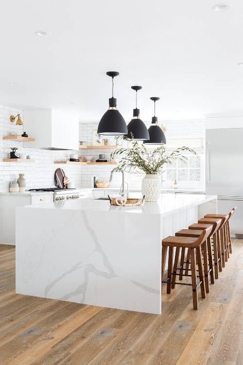 a white kitchen with sleek cabinets, floating shelves, a white marble kitchen island and black pendant lamps