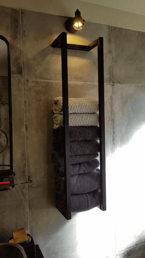 an industrial black metal wall-mounted shelf with various towels and a light over it is a stylish idea to store stuff