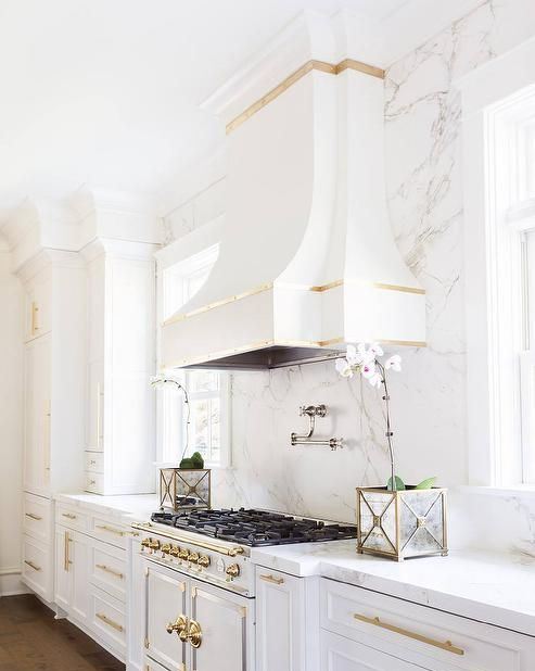 a super exquisite white vintage kitchen with a white marble wall and touches of gold looks very elegant and chic