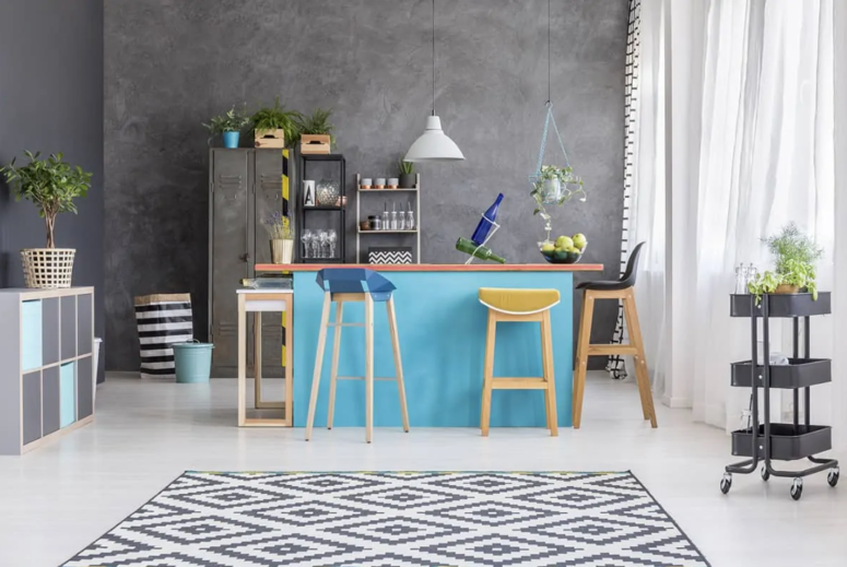 a small bright kitchen with a blue kitchen island and a set of mismatching colorful stools
