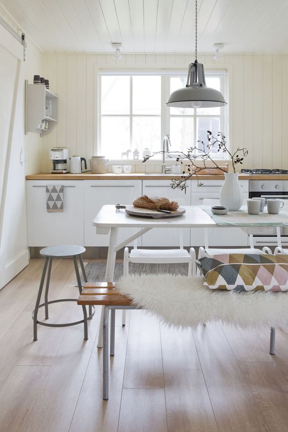 a Scandinavian kitchen with a white dining table and mismatching benches, chairs and stools