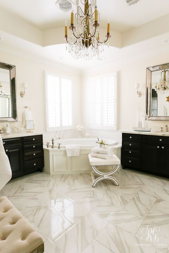 a refined white bathroom with a white marble floor, black furniture, a crystal chandelier and statement mirrors