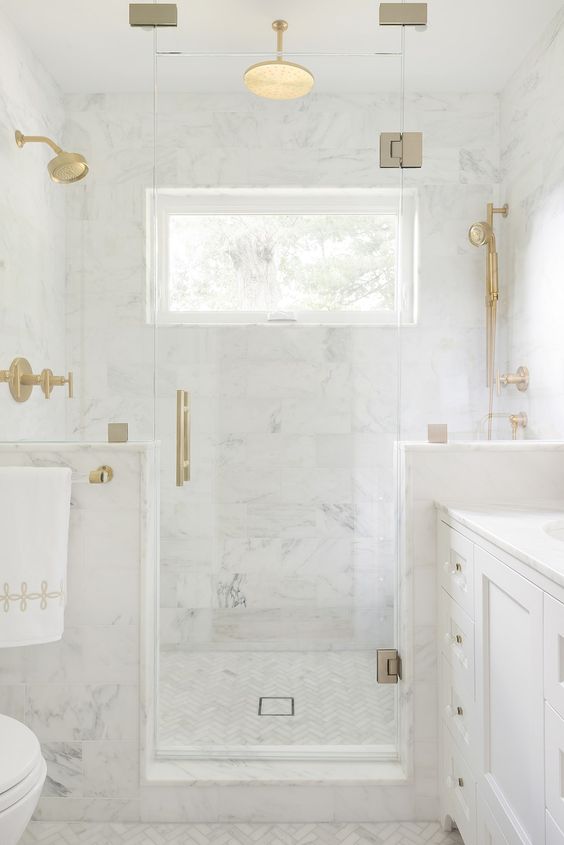 a glam bathroom clad with white marble tiles completely, with large scale tiles on the walls and herringbone ones on the floor