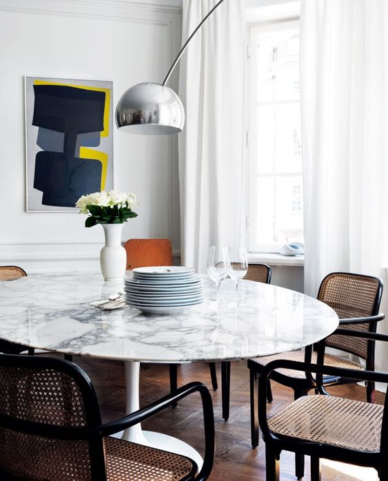 a chic white marble round dining table and rattan and cane chairs make up a chic mid-century modern dining zone