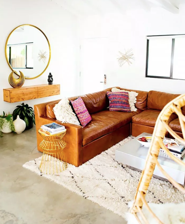 a boho living room done in neutrals, with a brown leather sofa, a floating vanity, a gold framed round mirror and touches of moon and stars
