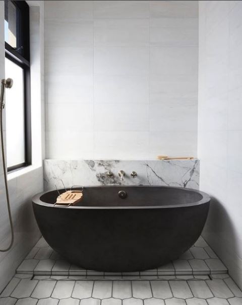 a chic contemporary bathroom with large scale tiles, white marble and concrete plus a black stone tub that wows