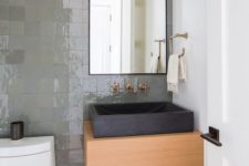 a contemporary bathroom with a shiny grene tile wall, a wooden vanity, a black square stone sink and a black framed mirror
