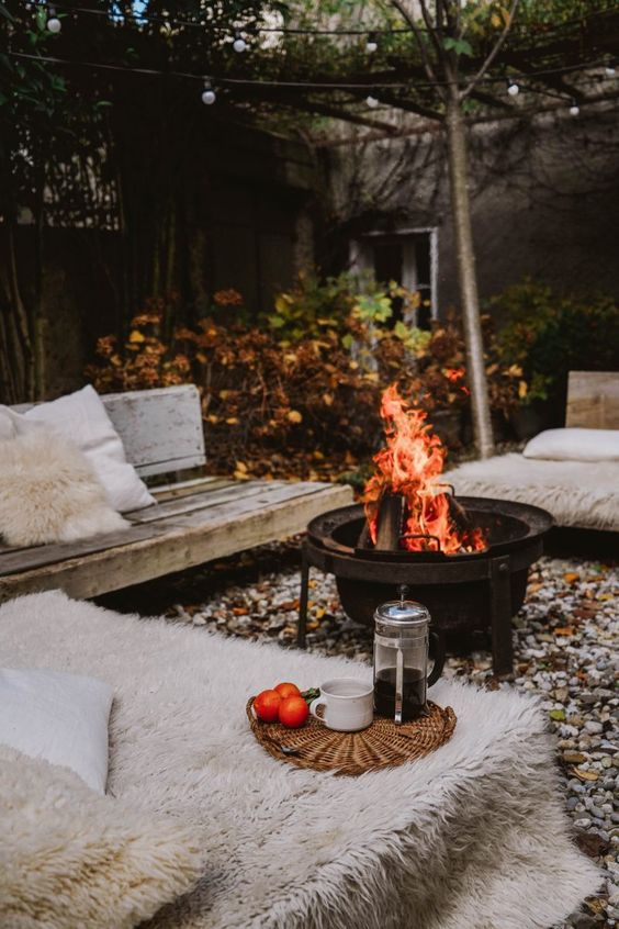 a fall backyard with wooden benches, faux fur, a fire pit and some pillows is super welcoming