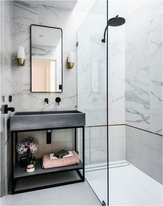 a glam bathroom clad with white marble, with tiles, a concrete sink and black fixtures to give it a fresher modern feel