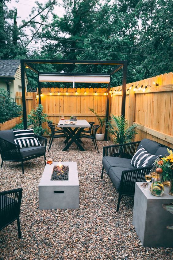 a mid-century modern backyard with gravel, a fire pit, black rattan furniture and lights all along the fence