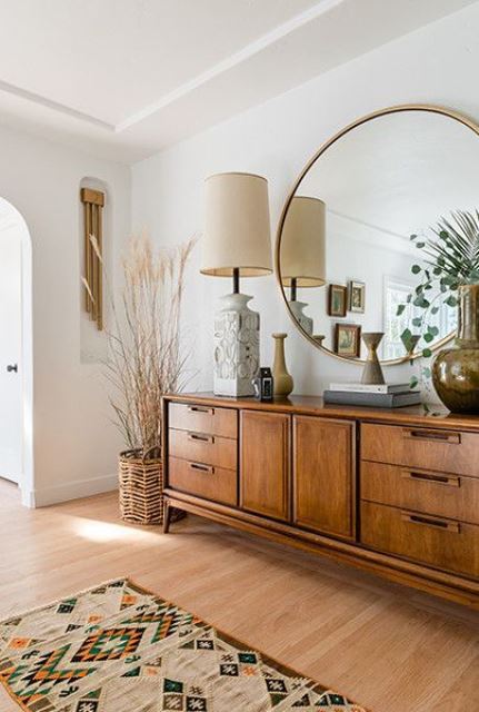 a mid-century modern living room with a wooden vanity, a large lamp, an oversized round mirror and some plants