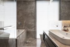 a minimalist bathroom clad with brown marble, with a logn sleek vanity and a marble clad bathtub is chic