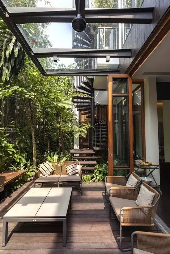 a modern tropical outdoor living room with metal and woven furniture, a wooden table and lots of greenery growing around