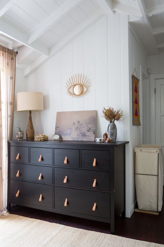 a neutral bedroom accented with a black dresser with leather pulls that highlights the color scheme and makes it cooler