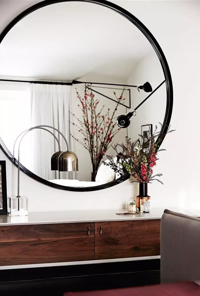 a refined living room with white walls, dark vintage-indpisred furniture and an oversized round mirror that fills the space with natural light