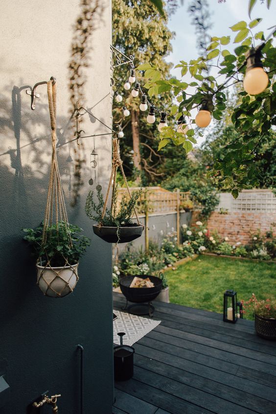 a small Nordic backyard with a black deck, a fire pit, candle lanterns, a green lawn and lots of blooms